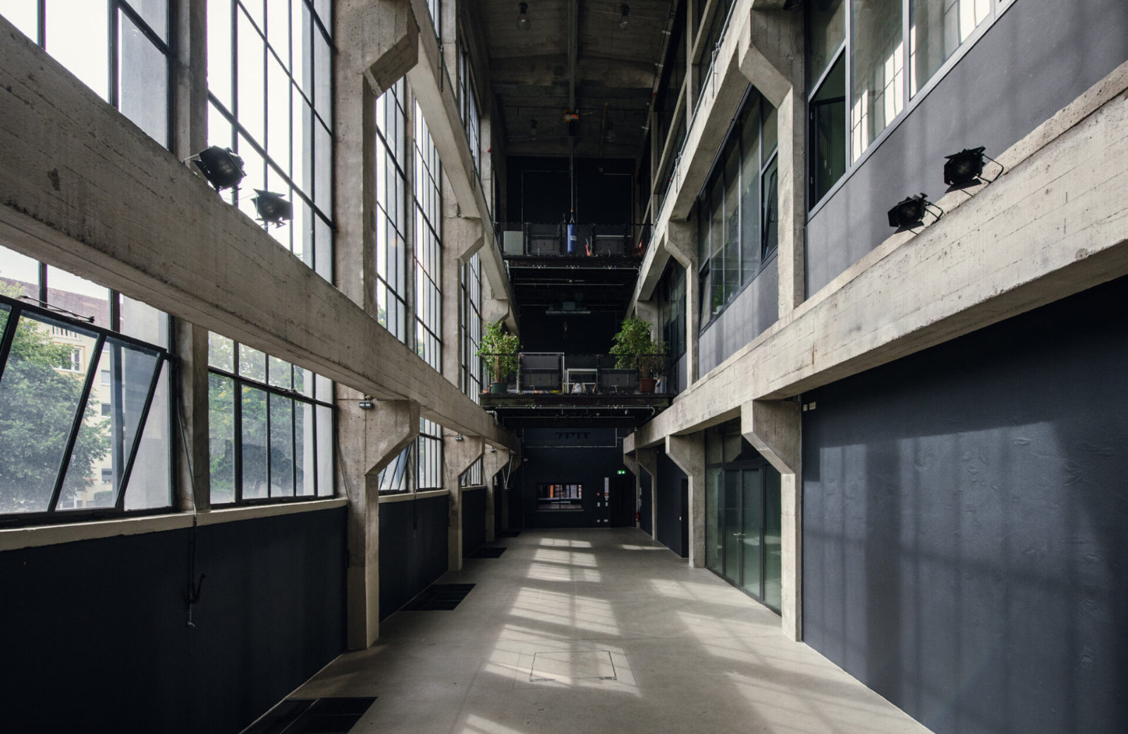 Foto: Industrieller Veranstaltungsraum mit hohen Decken, großen Fenstern und Betonwänden.