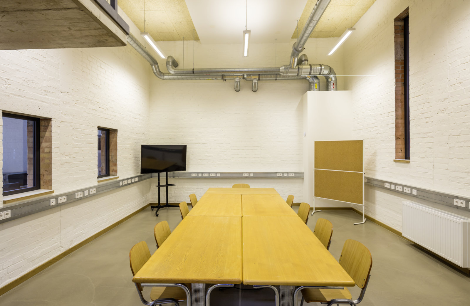 Foto: Moderner Besprechungsraum mit rechteckigem Holztisch, Holzstühlen, Monitor und weiß gestrichenen Wänden.