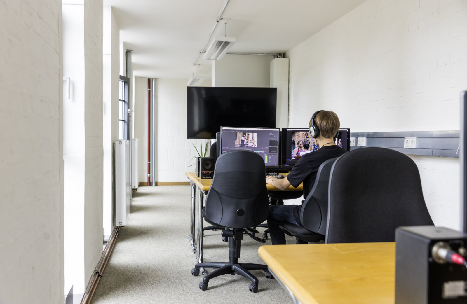 Foto: Ein Arbeitsplatz mit zwei Monitoren, an dem eine Person mit Kopfhörern an einem PC arbeitet.