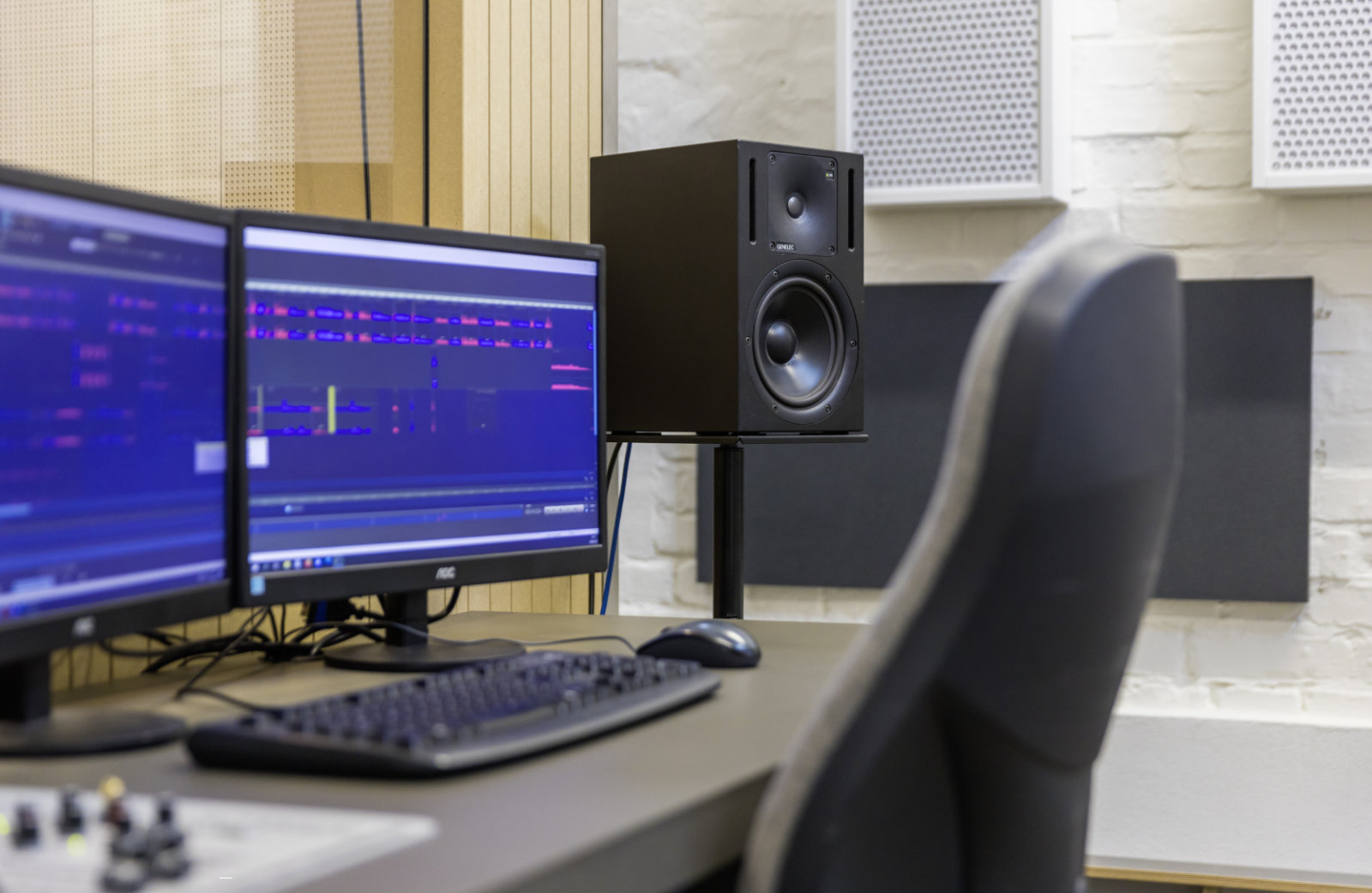 Foto: Zwei Monitore mit Audiobearbeitungssoftware, ein großer Lautsprecher und eine Tastatur auf dem Schreibtisch.